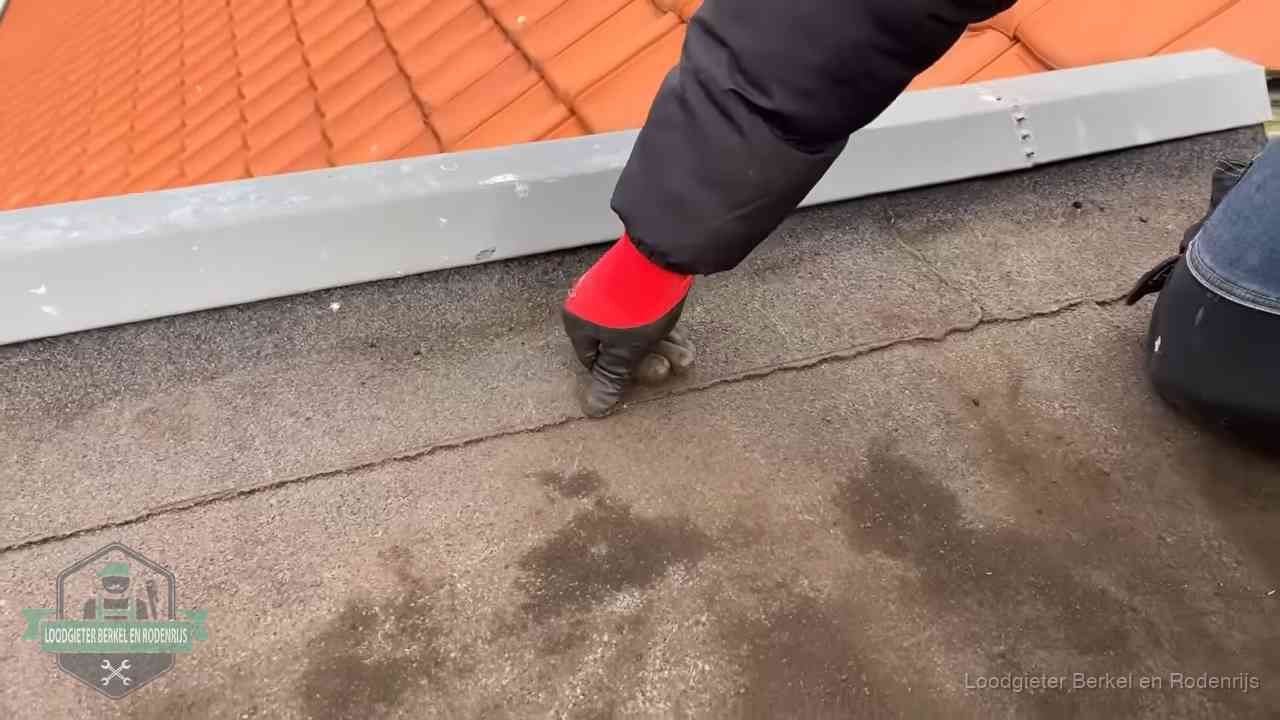Vakman wijst een naad met vochtplekken aan op een bitumen plat dak in Berkel en Rodenrijs