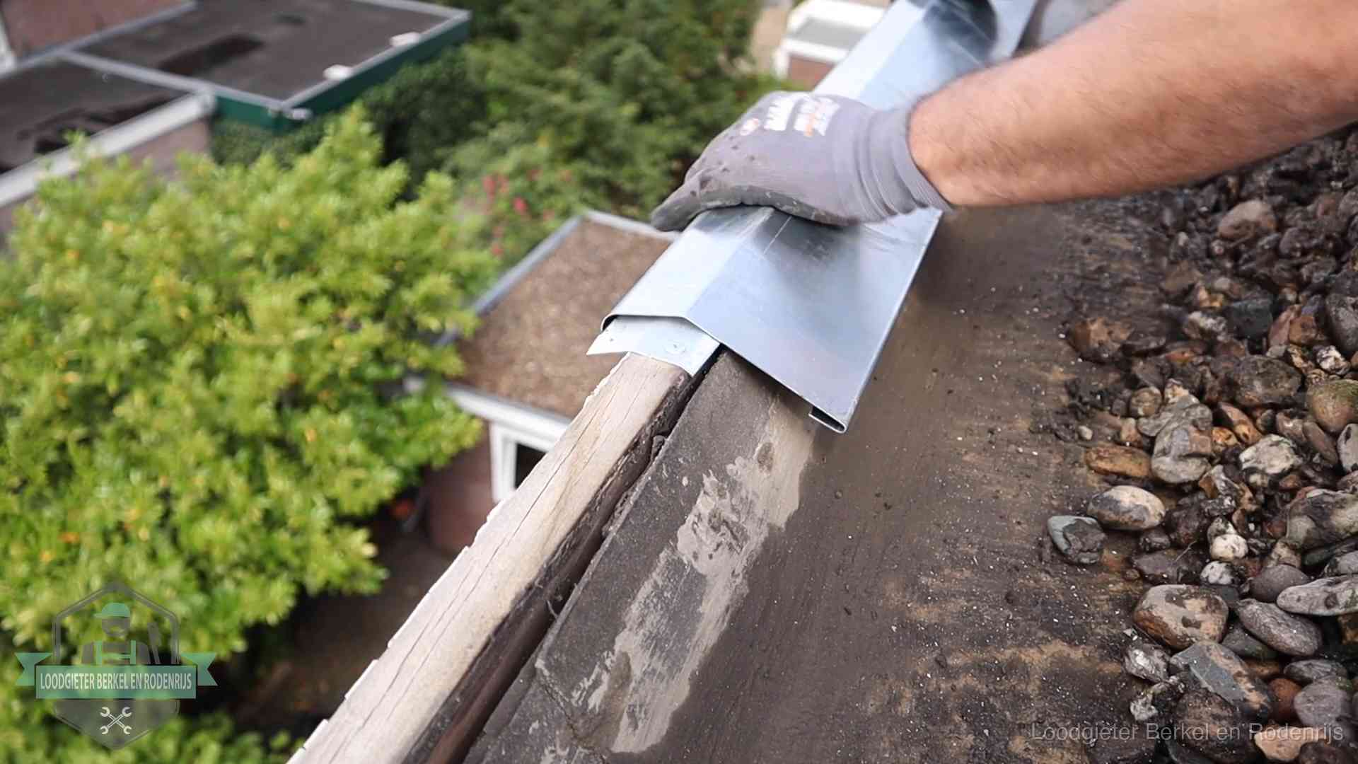 Dakdekker plaatst een zinken deklijst op een dakrand met uitzicht over een woonwijk in Berkel en Rodenrijs